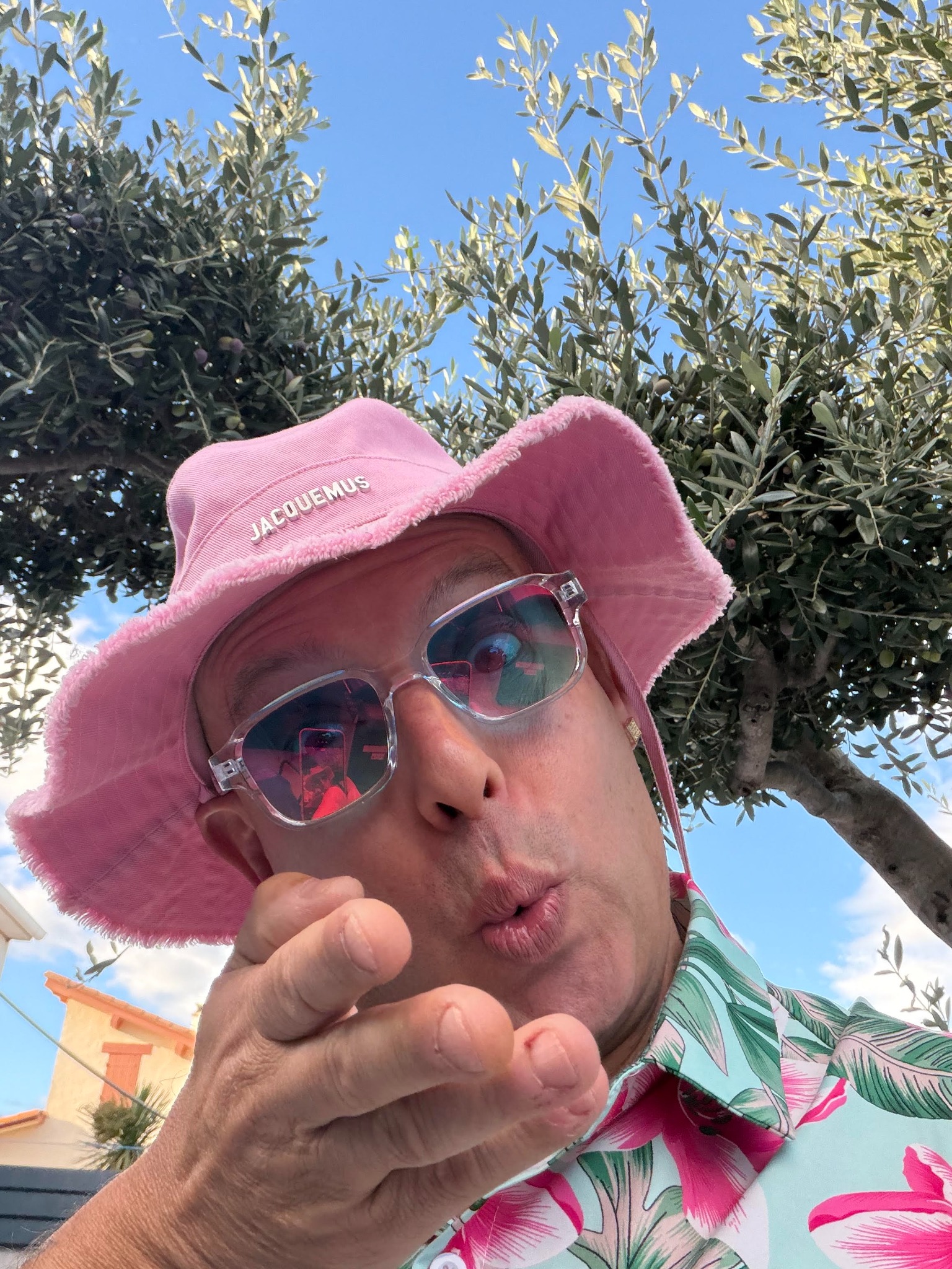 Can Cyssou avec son chapeau rose et ses lunettes, devant un olivier